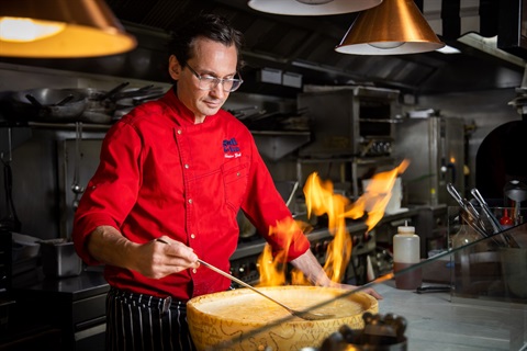 Chef with cheese wheel in flames in kitchen